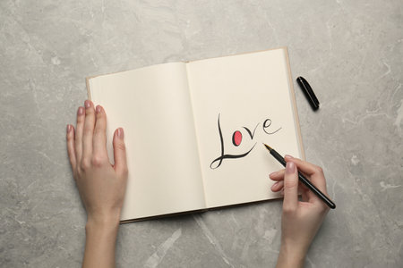 Woman writing word Love in notebook at light gray table, top viewの写真素材
