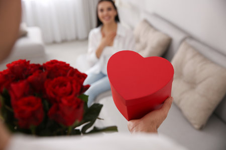 Man presenting gift and bouquet to his beloved woman at home, closeup. Valentine's day celebrationの写真素材