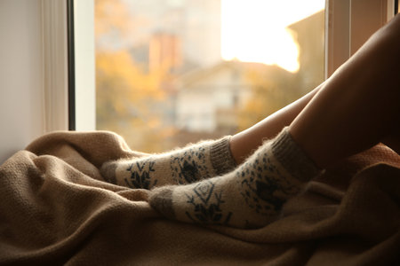 Woman in knitted socks relaxing on plaid near window at home, closeupの写真素材