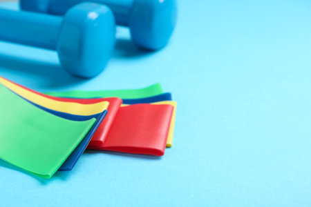 Fitness elastic bands and dumbbells on light blue background, closeup. Space for textの写真素材