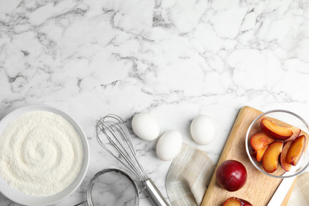 Fresh eggs and other ingredients on white marble table, flat lay with space for text. Cooking of delicious plum cakeの写真素材