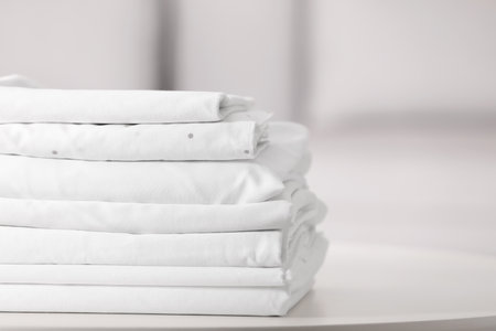 New clean folded bed linens on table indoors. Space for textの写真素材