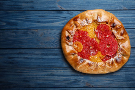 Delicious galette with citrus fruits on blue wooden table, top view. Space for text