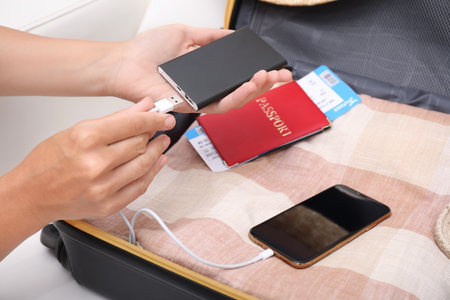Woman charging smartphone with power bank near packed suitcase indoors, closeupの写真素材