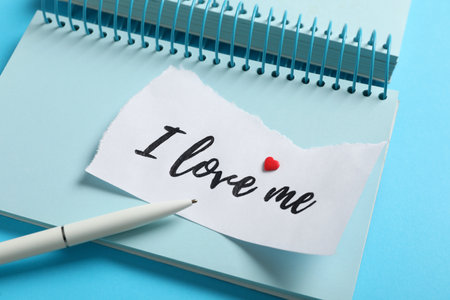 Paper with handwritten phrase I Love Me, notebook and pen on light blue background, closeupの写真素材