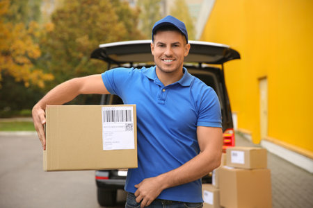 Courier with parcel near delivery van outdoorsの写真素材