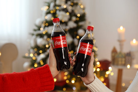 MYKOLAIV, UKRAINE - January 01, 2021: Women with bottles of Coca-Cola against blurred Christmas...