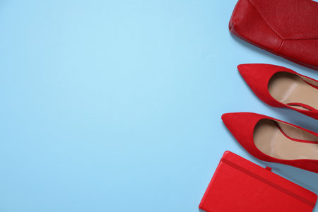 Red shoes, bag and notebook on light blue background, flat lay. Space for textの写真素材