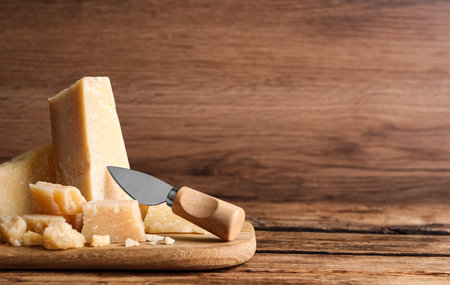 Pieces of delicious parmesan cheese with knife on wooden table. Space for textの写真素材