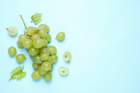 Bunch of ripe grapes with green leaves on light blue background, flat lay. Space for textの写真素材