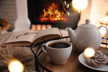 Cup of tea, cookies and book near fireplace indoors. Cozy atmosphereの写真素材