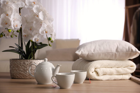 Beautiful orchid, teapot and cups of tea on table indoorsの写真素材