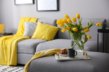 Tray with beautiful tulips on sofa indoors. Interior design in gray and yellow colorsの写真素材