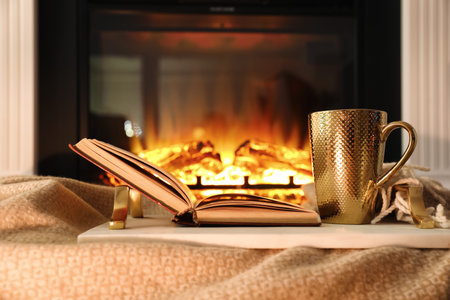 Cup of hot drink and book on blanket near fireplace indoors. magic atmosphereの写真素材