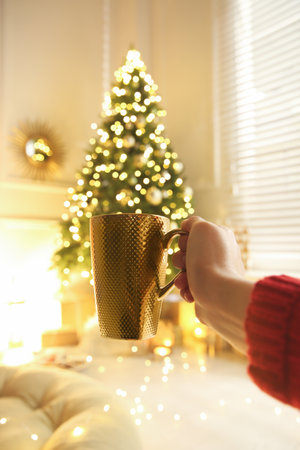 Woman with cup of drink and blurred Christmas tree on background, closeupの写真素材