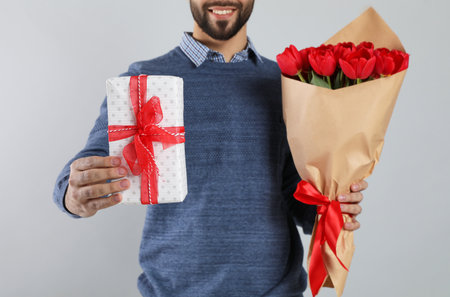 Happy man with red tulip bouquet and gift box on light gray background, closeup. 8th of March celebrationの写真素材