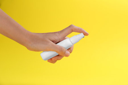 Woman with bottle of insect repellent spray on yellow background, closeupの写真素材
