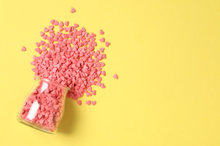 Bright heart shaped sprinkles and glass jar on yellow background, flat lay. Space for textの写真素材