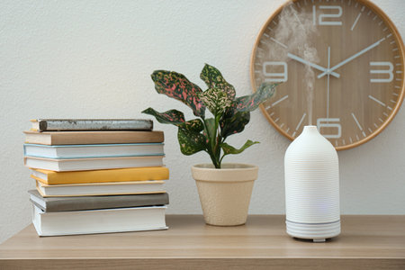 Aroma oil diffuser, plant and books on wooden table indoors. interior design