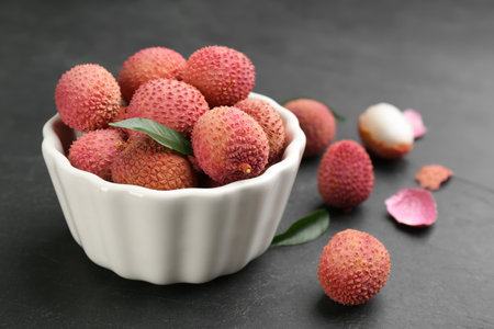 Fresh ripe lychee fruits in white ceramic bowl on black tableの写真素材