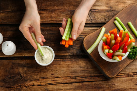 Woman dipping celery stick in sauce on wooden table, top viewの写真素材