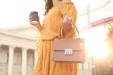 Young woman with stylish brown bag and cup of coffee on city street, closeupの写真素材