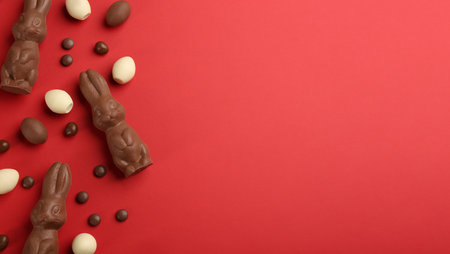 Flat lay composition with chocolate Easter bunnies, eggs and candies on red background. Space for textの写真素材