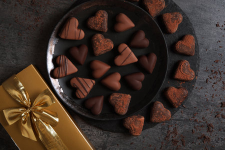 Delicious heart shaped chocolate candies and gift box on gray table, flat layの写真素材