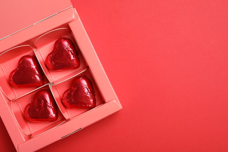 Tasty chocolate heart shaped candies in pink box on red background, top view. Space for textの写真素材