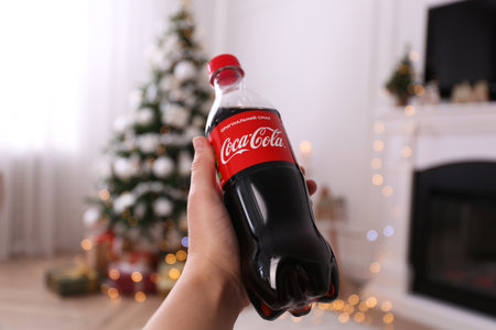 MYKOLAIV, UKRAINE - JANUARY 13, 2021: Woman holding bottle of Coca-Cola in room with Christmas tree,...
