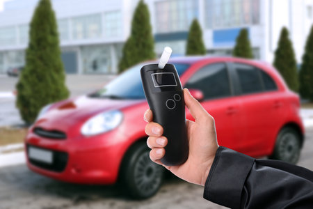 Police officer with breathalyser near car outdoors. Alcohol consumption while drivingの写真素材