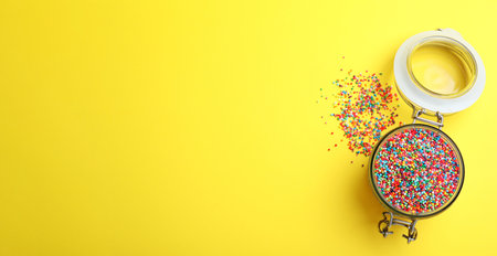Colorful sprinkles in jar on yellow background, flat lay with space for text. Confectionery decorの写真素材