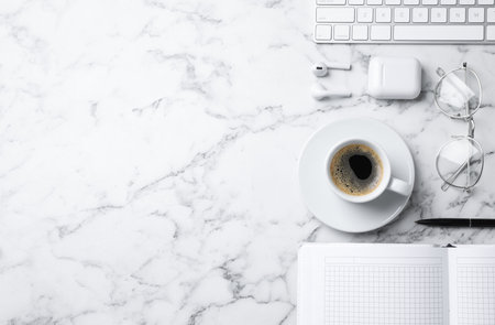 Flat lay composition with cup of coffee, earphones and stationery on white marble tableの写真素材