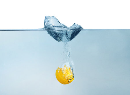 Ripe lemon falling down into clear water with splashes against beige backgroundの写真素材