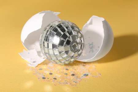 Silver disco ball, broken eggshell and glitter sprinkles on yellow background, closeupの写真素材
