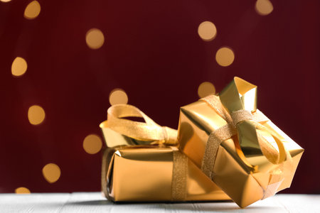 Golden gift boxes against red background with blurred lights, space for textの写真素材