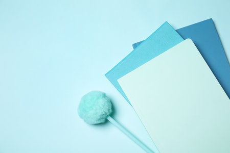 Pen with pompom and notebooks on light blue background, flat lay. Space for textの写真素材