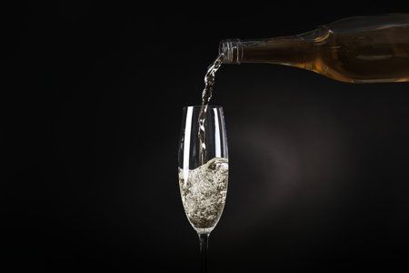 Pouring sparkling wine from bottle into glass on black backgroundの写真素材