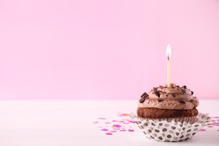 Chocolate cupcake with burning candle on white table against pink background. Space for textの写真素材