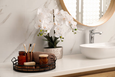 Beautiful flowers and different toiletries near vessel sink in bathroomの写真素材