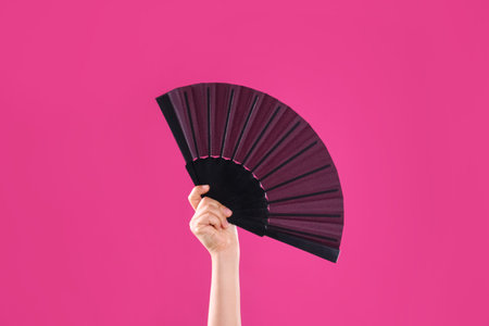 Woman holding black hand fan on pink background, closeupの写真素材