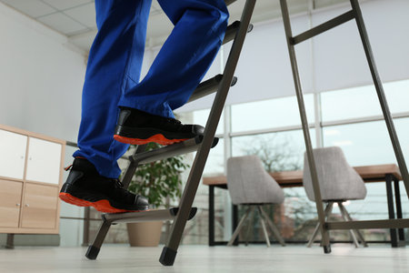 Professional worker climbing up ladder in room, closeup. Space for textの写真素材