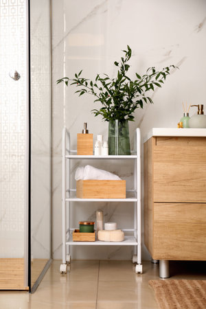 Vase with green branches and different toiletries on rack in bathroomの写真素材