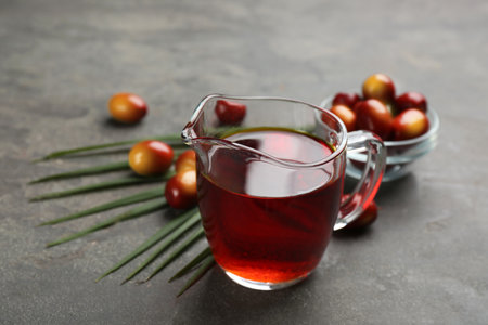Palm oil in glass jug, tropical leaf and fruits on gray tableの写真素材