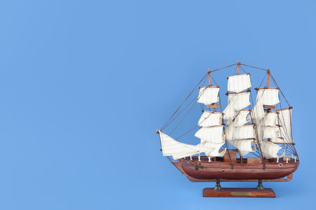 Miniature model of old ship with white sails on blue background, space for textの写真素材