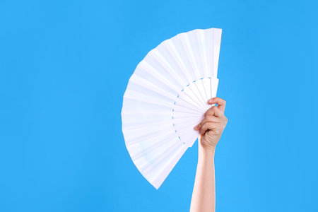 Woman holding white hand fan on light blue background, closeupの写真素材