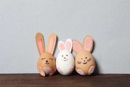Eggs as cute bunnies on wooden table against light gray background, space for text. easter...