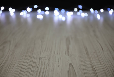 Blurred view of beautiful glowing lights, focus on wooden table. Space for textの写真素材