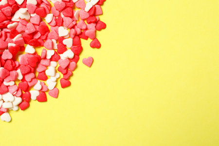 Bright heart shaped sprinkles on yellow background, flat lay. Space for textの写真素材