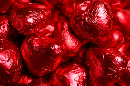 Tasty chocolate heart shaped candies in red foil wrappers as background, closeupの写真素材